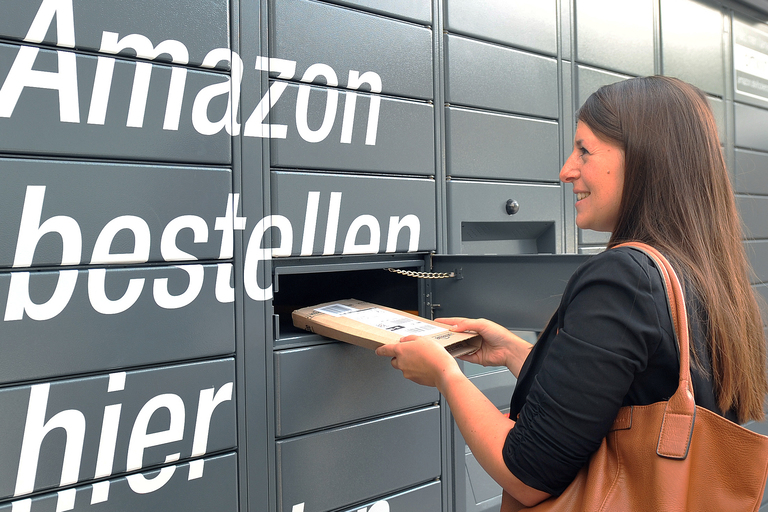 Frau steht vor Amazon Locker mit Paket in der Hand
